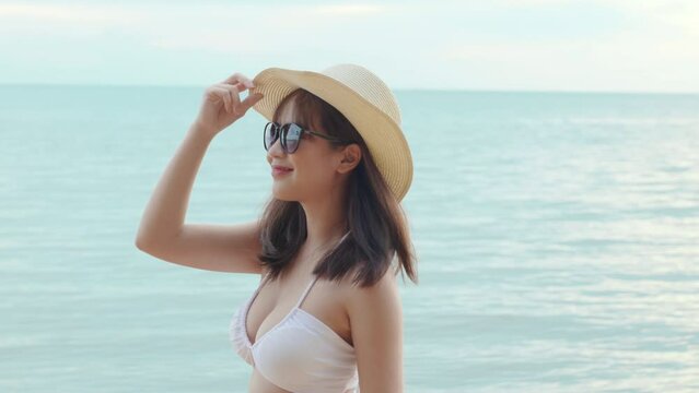 Beautiful Asian woman wear sungrass and hat turning back to looking camera and smiling at beach, Portrait of happy female in bikini having fun laughing on tropical in summer holiday