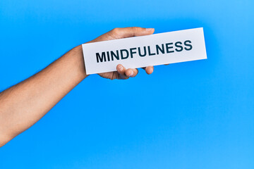 Hand of caucasian man holding paper with mindfulness word over isolated blue background