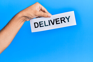 Hand of caucasian man holding paper with delivery word over isolated blue background