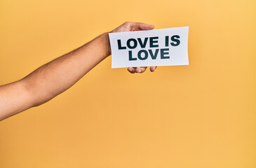 Hand of caucasian man holding paper with love is love message over isolated yellow background