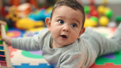 Adorable hispanic baby lying on floor with relaxed expression at kindergarten