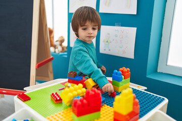 Adorable toddler playing with construction blocks standing at kindergarten