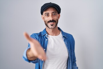 Hispanic man with beard standing over isolated background smiling cheerful offering palm hand giving assistance and acceptance.