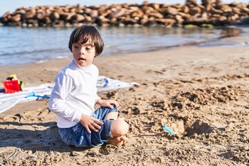 Down syndrome kid playing with relaxed expression sitting on sand at beach