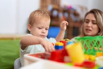 Fototapeta premium Teacher and toddler playing with construction blocks sitting on table at kindergarten