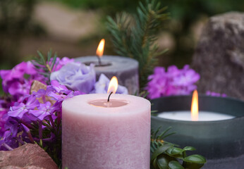 Obraz na płótnie Canvas Closeup burning candles purple flowers stone on blurred background. Focus on light candlewick. Beautiful composition with violet candles for spa treatment. Zen relax memorial concept.