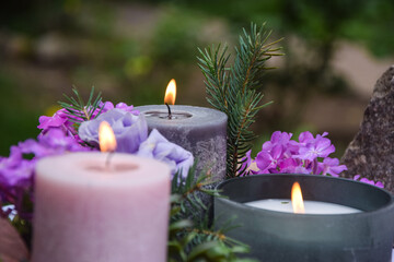 Obraz na płótnie Canvas Closeup burning candles purple flowers stone on blurred background. Selective focus on light candlewick. Beautiful composition with violet candles for spa treatment. Zen relax memorial concept.