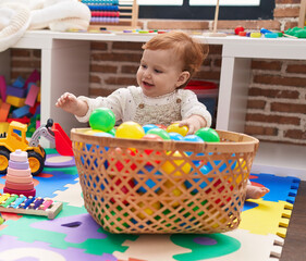 Adorable redhead toddler playing with balls sitting on floor at kindergarten