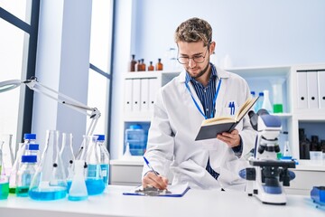 Young man scientist writing report reading book at laboratory