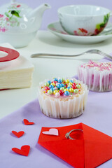 Valentine's Day template, surprise  tea party, birthday background, red envelope, hearts, gift ring, cheesecake with sprinkle balls, closeup, vertical photo. Holiday breakfast with cake, white tea set