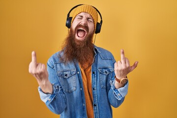 Caucasian man with long beard listening to music using headphones showing middle finger doing fuck...