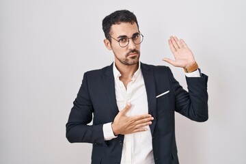 Handsome business hispanic man standing over white background swearing with hand on chest and open palm, making a loyalty promise oath