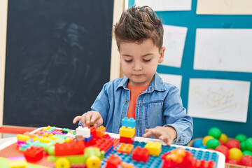 Adorable hispanic toddler playing with construction blocks sitting on table at kindergarten