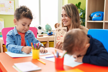 Fototapeta premium Teacher with boys sitting on table having language lesson at kindergarten