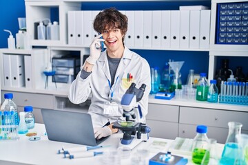 Young hispanic man scientist talking on the smartphone using laptop at laboratory