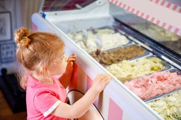 Cute little toddler girl choosing and buying ice cream in a cafe. Happy baby child looking at...