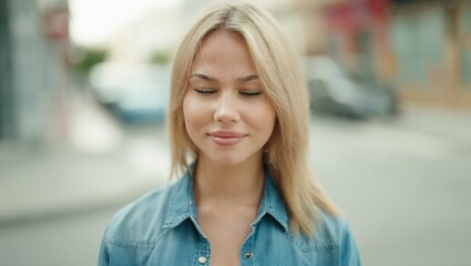 Young blonde woman smiling confident with close eyes at street