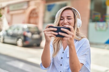 Fototapeta premium Young blonde woman smiling confident watching video on smartphone at street