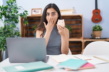 Young teenager girl studying using computer laptop covering mouth with hand, shocked and afraid for...