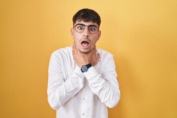 Young hispanic man standing over yellow background shouting suffocate because painful strangle. health problem. asphyxiate and suicide concept.