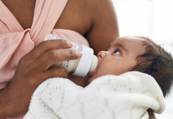 African american baby sucking feeding bottle at bedroom
