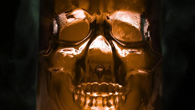 Brown Skull Boils Poisonously. Bright, rich gold glass vessel in the form of the skull, from which are evaporation and slow down the edges on a black background