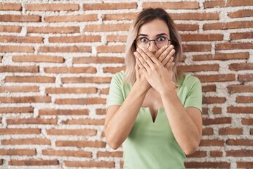 Young beautiful woman standing over bricks wall shocked covering mouth with hands for mistake....