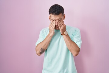 Handsome hispanic man standing over pink background rubbing eyes for fatigue and headache, sleepy...