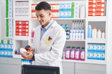 Naklejka na ściany i meble Young hispanic man pharmacist scanning pills bottle at pharmacy