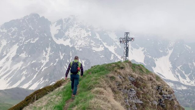 A man reaches the top of the mountain, where there is a metal crucifix with Tibetan flags attached, and looks at the view.
He is wearing sports equipment