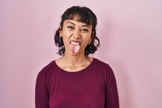 Young beautiful woman standing over pink background sticking tongue out happy with funny expression. emotion concept.