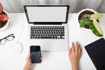 Female sitting workspace using hand holding black smartphone blank screen mock up on a table with laptop computer, female hold mobile phone with notebook at office