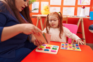 Fototapeta premium Teacher and student playing with maths puzzle game looking cards at kindergarten