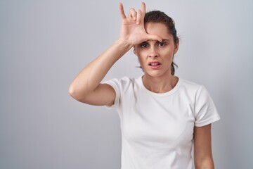 Beautiful brunette woman standing over isolated background making fun of people with fingers on...