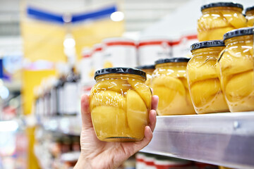 Canned peaches in glass jar in the hands in store