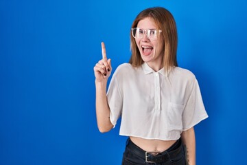 Beautiful woman standing over blue background pointing finger up with successful idea. exited and happy. number one.