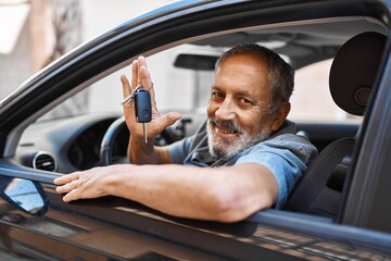 Senior grey-haired man smiling confident holding key of new car at street