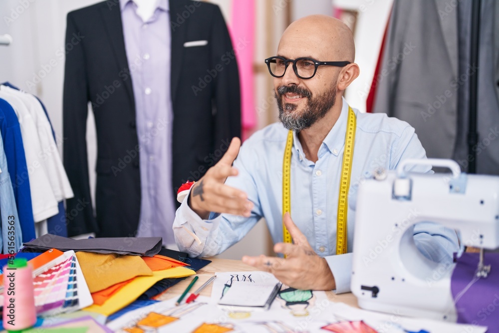 Sticker Young bald man tailor smiling confident speaking at tailor shop