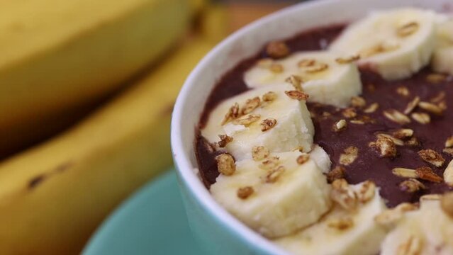 A&ccedil;a&iacute; congelado na tigela com banana e granola sobre uma t&aacute;bua de madeira. Comida brasileira, sobremesa