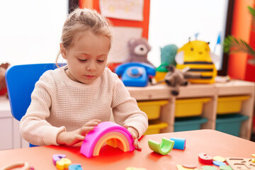 Adorable blonde girl playing with toys sitting on table at kindergarten