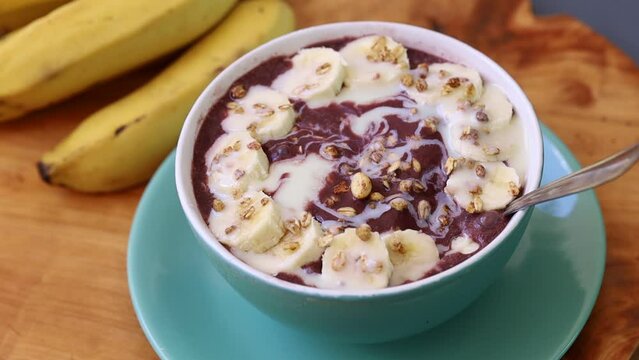 A&ccedil;a&iacute; congelado na tigela com banana, granola e leite condensado sobre uma t&aacute;bua de madeira. Comida brasileira, sobremesa.