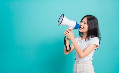Portrait Asian beautiful young woman standing smile holding and shouting into megaphone looking to space, shoot the photo in a studio on a blue background, There was copy space