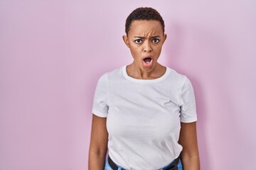 Beautiful african american woman standing over pink background in shock face, looking skeptical and sarcastic, surprised with open mouth