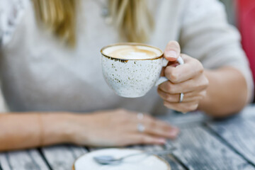 Closeup of hands of woman drinking cappuccino and cup of coffee while waiting for friend and breakfast. Happy alone woman in outdoor cafe or restaurant on sunny summer day.