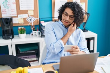 Young latin man business worker talking on smartphone reading reminder paper at office
