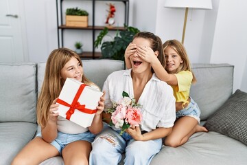 Mother and daughters smiling confident suprise with gift and flowers at home