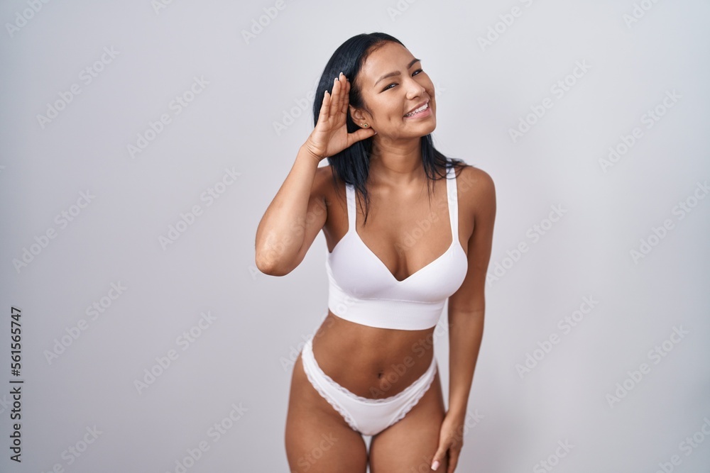 Wall mural hispanic woman wearing lingerie smiling with hand over ear listening an hearing to rumor or gossip. 