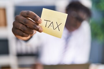 African american man business worker holding reminder paper with tax message at office
