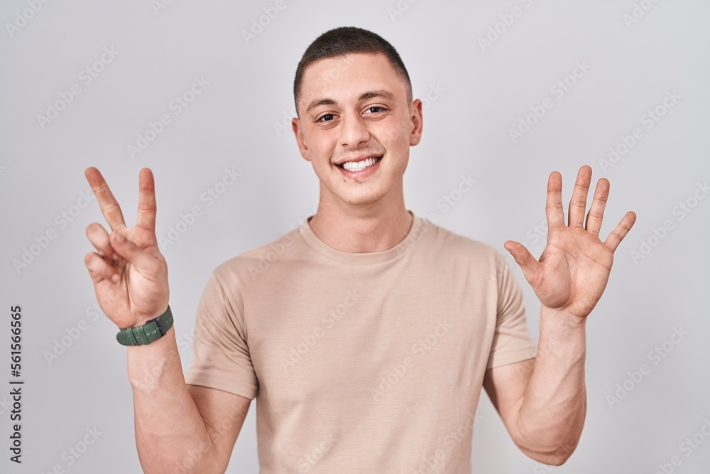 Wall mural Young man standing over isolated background showing and pointing up with fingers number seven while smiling confident and happy.