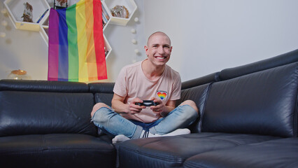 Smiling gay man playing video games with a controller indoor. High quality photo